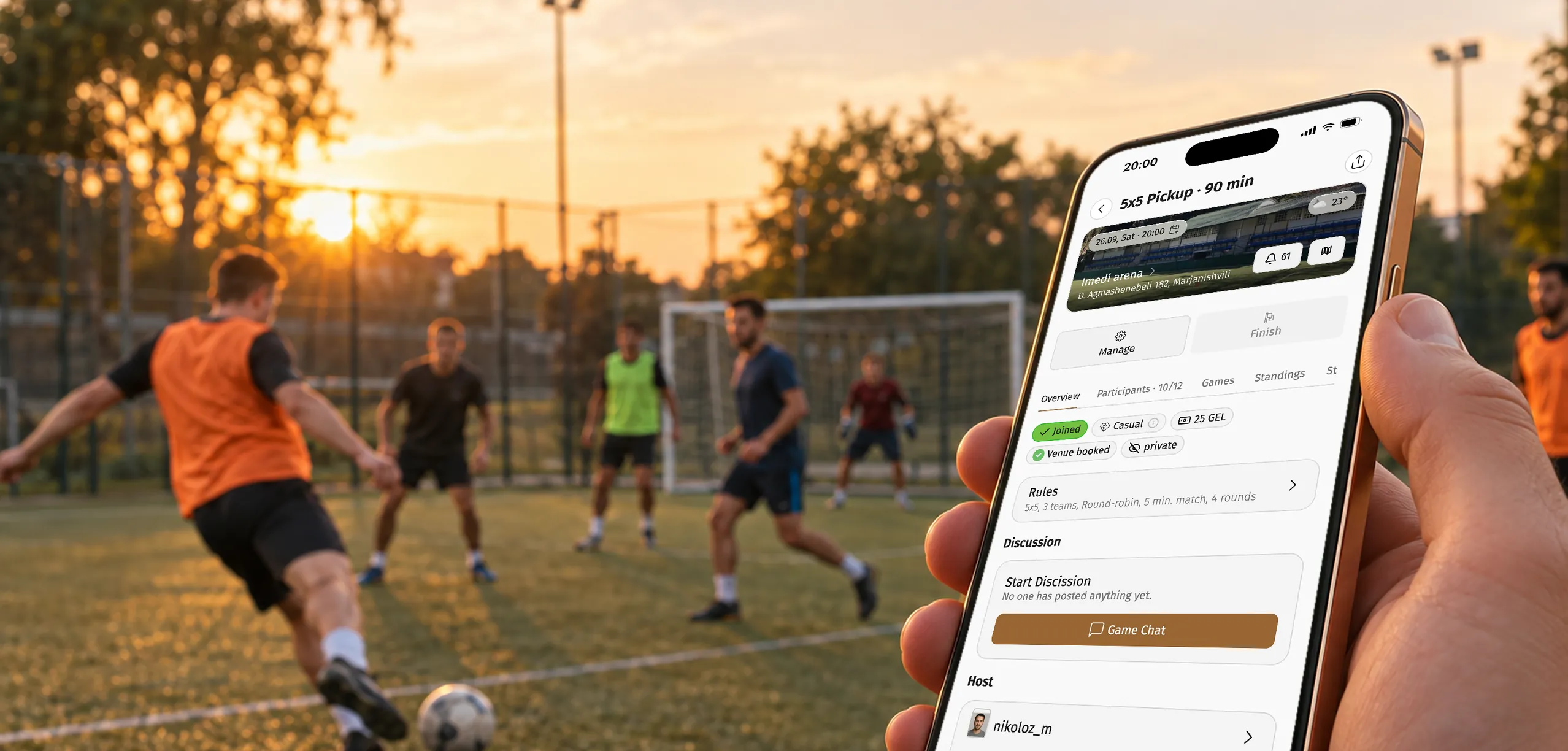 Organizer holding a phone with the Playbox game lobby while players run for the ball on a pitch at sunset