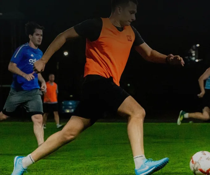 Player in an orange bib striking the ball during an evening pickup football game