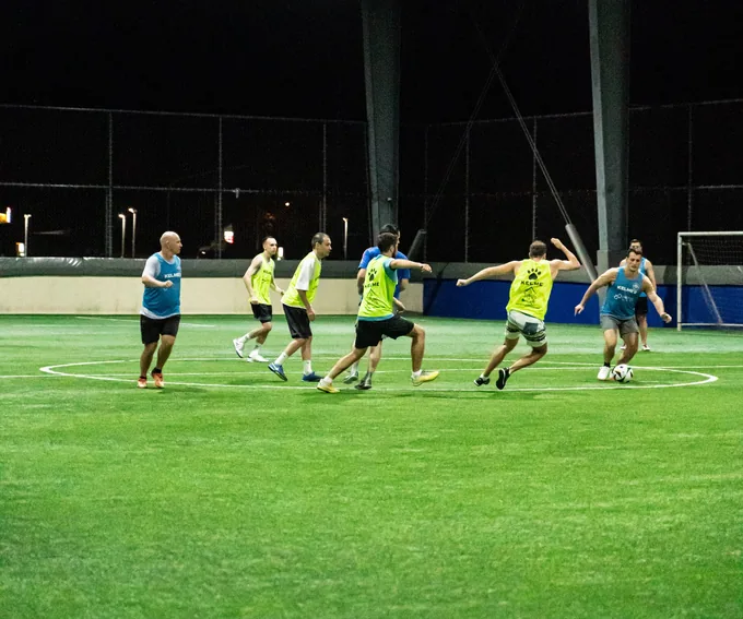 Players running for the ball in an evening five-a-side game on an artificial pitch